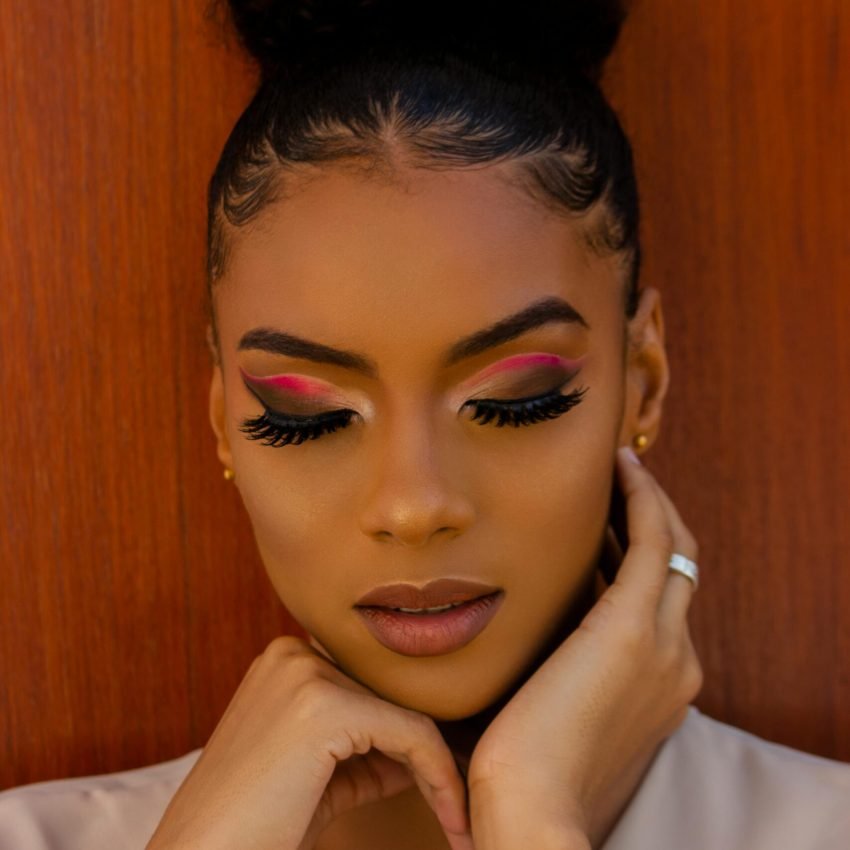 Close-up portrait of a woman with elegant hairstyle and vibrant eye makeup against a wooden background.